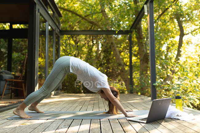 Азиатка практикует йогу с помощью ноутбука на террасе в саду. в доме в изоляции во время карантинной изоляции. — стоковое фото