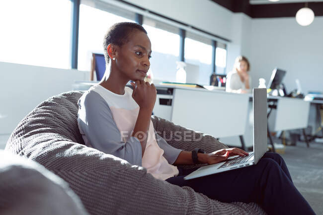 Afroamerikanische Geschäftsfrau sitzt im Sessel und benutzt Laptop bei der Arbeit. unabhängiges kreatives Geschäft in einem modernen Büro. — Stockfoto