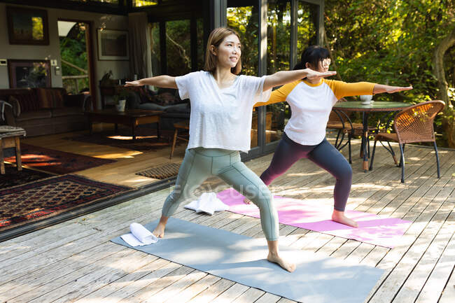 Asiatische Mutter und ihre Tochter praktizieren Yoga auf der Terrasse im Garten. Zuhause in Isolation während der Quarantäne. — Stockfoto
