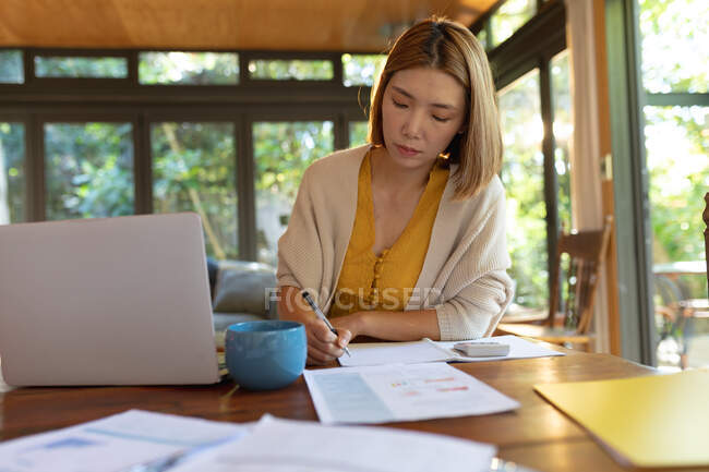 Asian woman making notes sitting at table, working from home. at home in isolation during quarantine lockdown. — Stock Photo