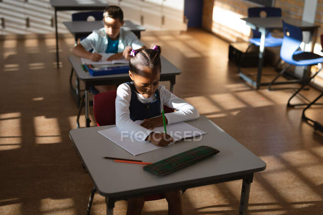 Ragazza afroamericana che studia mentre si siede sulla scrivania in classe alle elementari. concetto di scuola e istruzione — Foto stock
