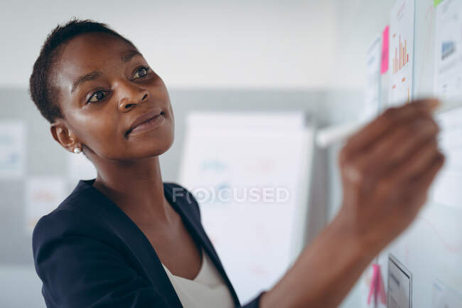 Африканська бізнесменка-американка робить нотатки і додає столи на стіні. Незалежний творчий бізнес у сучасному офісі.. — стокове фото