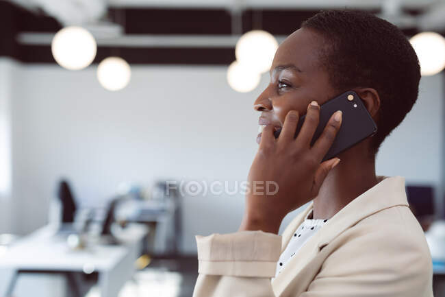 Lächelnde afrikanisch-amerikanische Geschäftsfrau mit Smartphone bei der Arbeit. unabhängiges kreatives Geschäft in einem modernen Büro. — Stockfoto