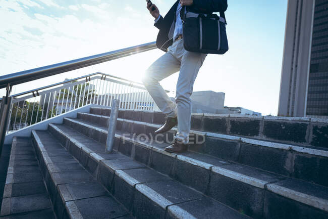 Midsection of businessman using smartphone walking down steps in city street. digital nomad out and about in city concept. — Stock Photo