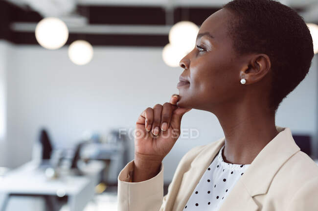 Femme d'affaires afro-américaine réfléchissant, touchant le menton au travail. entreprise créative indépendante dans un bureau moderne. — Photo de stock