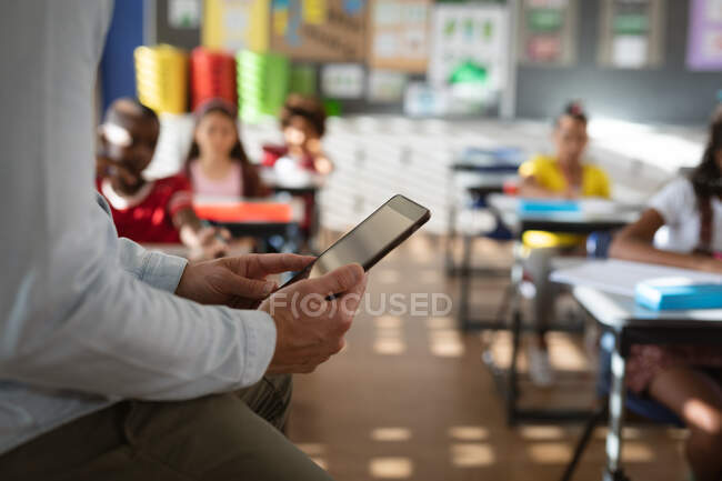 Середня частина вчителя чоловічої статі використовує цифровий планшет, сидячи в класі в початковій школі. концепція школи та освіти — стокове фото