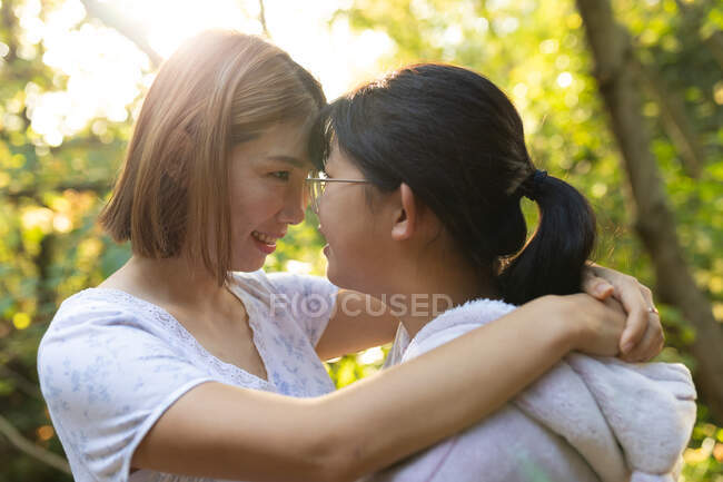 Porträt einer lächelnden asiatischen Frau mit ihrer Tochter, die Köpfe berührt und sich im Garten umarmt. Zuhause in Isolation während der Quarantäne. — Stockfoto