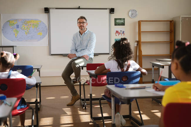 Portrait of caucasian male teacher teaching diverse group of students in class at elementary school. school and education concept — Stock Photo