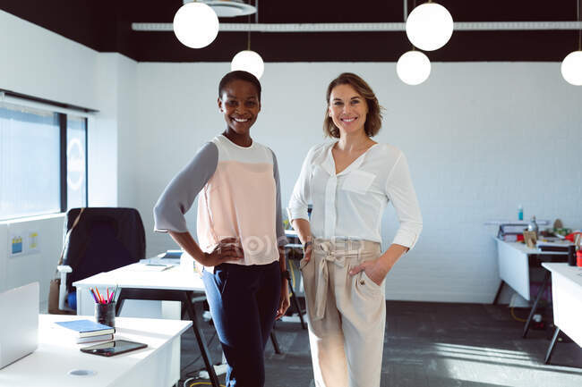 Duas mulheres de negócios sorrindo diversas que estão de pé e olhando para a câmera no trabalho. negócio criativo em um escritório moderno. — Fotografia de Stock