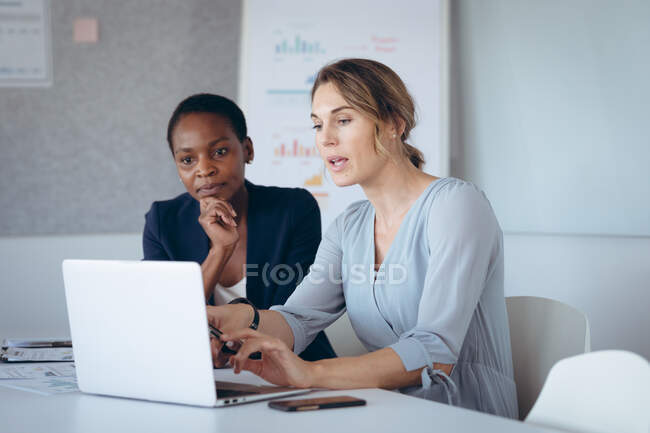Duas mulheres de negócios diversas sentadas na mesa, usando laptop, conversando. negócio criativo independente em um escritório moderno. — Fotografia de Stock