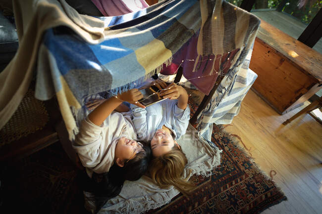 Sorrindo mulher asiática com sua filha usando tablet tomando selfie deitado sob a tenda cobertor. em casa em isolamento durante o confinamento de quarentena. — Fotografia de Stock
