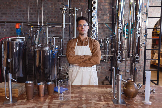Portrait of caucasian male worker wearing apron standing with arms crossed at gin distillery. alcohol production and filtration concept — Stock Photo