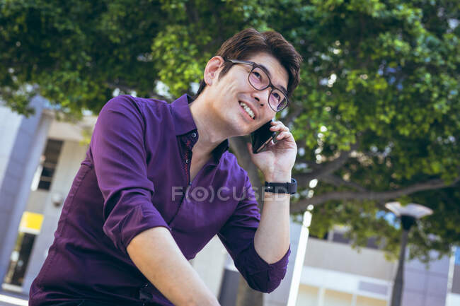 Улыбающийся азиатский бизнесмен, использующий смартфон на городской улице. цифровая реклама и концепция города. — стоковое фото