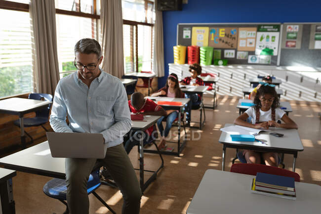 Кавказький вчитель чоловічої статі за допомогою ноутбука, коли сидів у класі в початковій школі. школа і освіта — стокове фото
