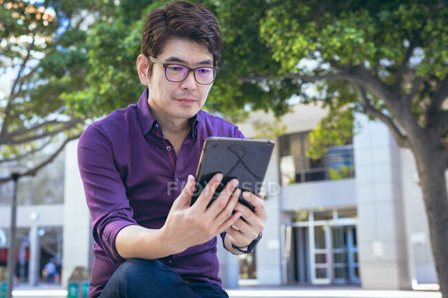 Sorridente uomo d'affari asiatico utilizzando tablet in strada della città. nomade digitale in giro per la città concetto. — Foto stock
