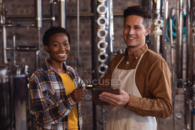 Портрет работника мужского и женского пола с цифровым планшетом, улыбающимся на заводе по производству джина. Концепция производства и фильтрации алкоголя — стоковое фото
