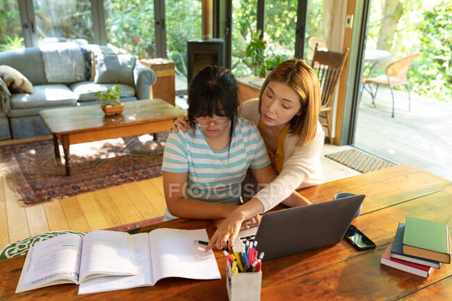 Chica asiática usando el ordenador portátil de aprendizaje en línea de su madre ayudándola. en casa en aislamiento durante el bloqueo de cuarentena. - foto de stock