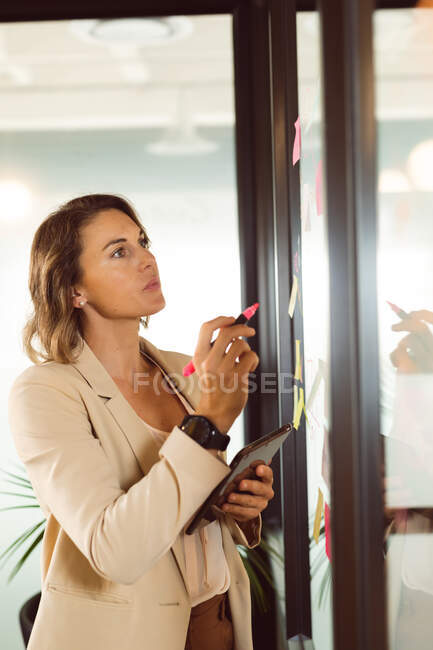 Caucasian businesswoman making notes and adding post-ins on transparent board. independent creative business at a modern office. — Stock Photo