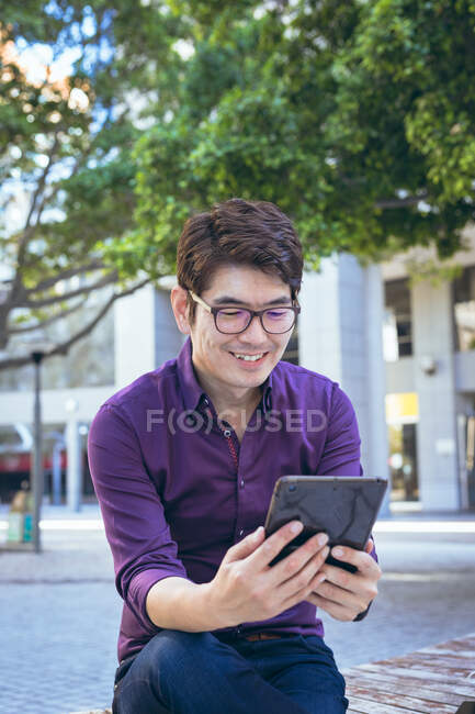 Улыбающийся азиатский бизнесмен, использующий планшет на городской улице. цифровая реклама и концепция города. — стоковое фото
