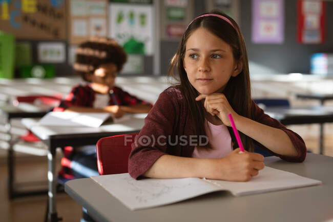 Белая девушка смотрит в окно, сидя на столе в классе в начальной школе. школа и концепция образования — стоковое фото