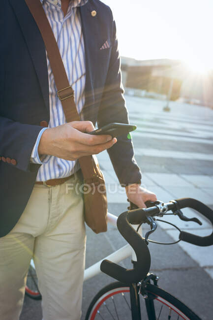 Мидсекция бизнесмена, использующего смартфон с велосипедом на городской улице. цифровая реклама и концепция города. — стоковое фото