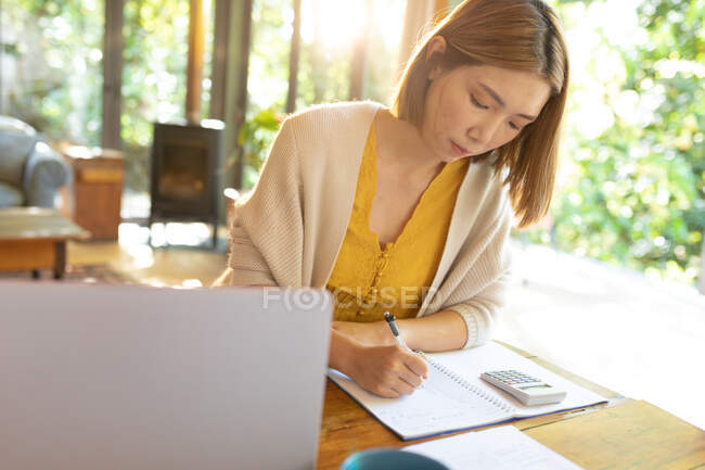 Asian woman making notes sitting at table, working from home. at home in isolation during quarantine lockdown. — Stock Photo