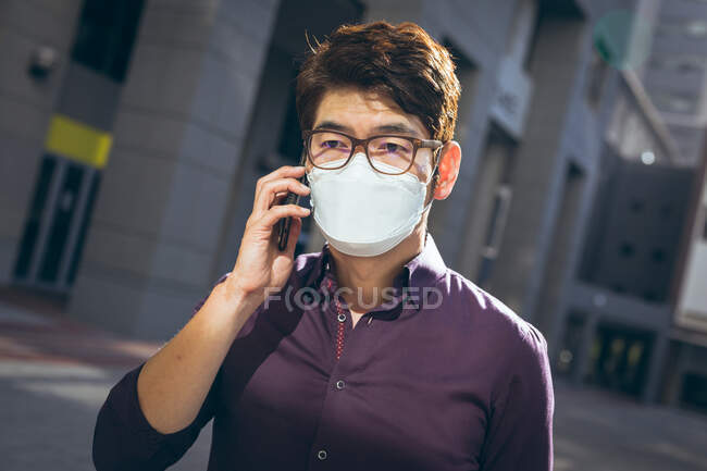 Homem de negócios asiático usando máscara facial usando smartphone na rua da cidade. nômade digital para fora e sobre na cidade durante covid 19 conceito pandêmico. — Fotografia de Stock