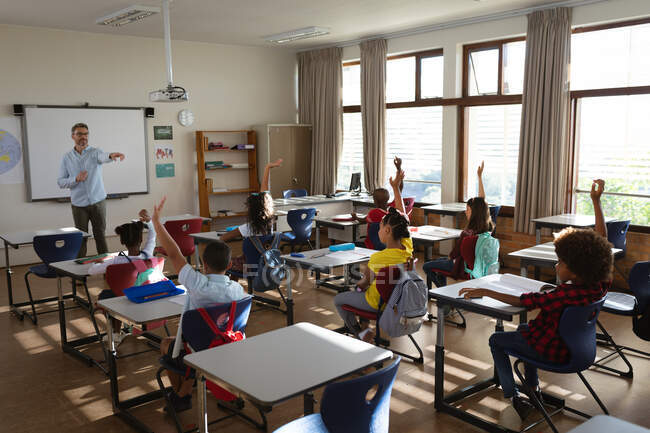 Group of diverse students raising their hands in the class at elementary school. school and education concept — Stock Photo