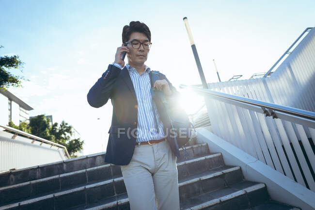 Азіатський бізнесмен, який розмовляє на смартфоні, йде по сходах на міській вулиці. Цифровий кочівник і про про про в міській концепції. — стокове фото