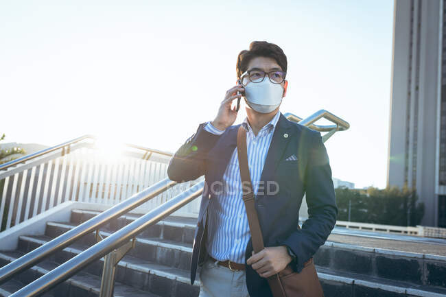 Hombre de negocios asiático con máscara facial usando smartphone en la calle de la ciudad. nómada digital en la ciudad durante el concepto covid 19 pandemia. - foto de stock