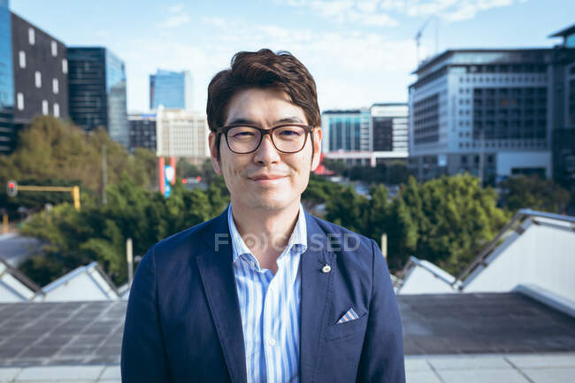 Retrato de homem de negócios asiático sorridente na rua da cidade com edifícios modernos atrás dele. homem de negócios em movimento e sobre no conceito de cidade. — Fotografia de Stock
