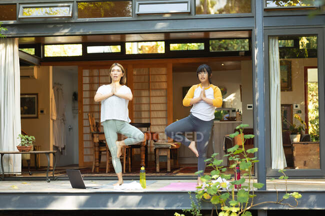 Femme asiatique et sa fille pratiquant le yoga en utilisant un ordinateur portable sur la terrasse dans le jardin. à domicile en isolement pendant le confinement en quarantaine. — Photo de stock