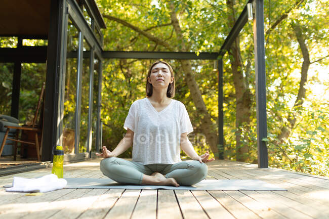 Asiatin praktiziert Yoga mit geschlossenen Augen auf der Terrasse im Garten. Zuhause in Isolation während der Quarantäne. — Stockfoto