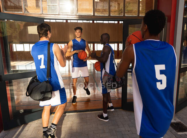 Разнообразная мужская баскетбольная команда держит мячи и разговаривает. баскетбол, спортивные тренировки на крытой площадке. — стоковое фото