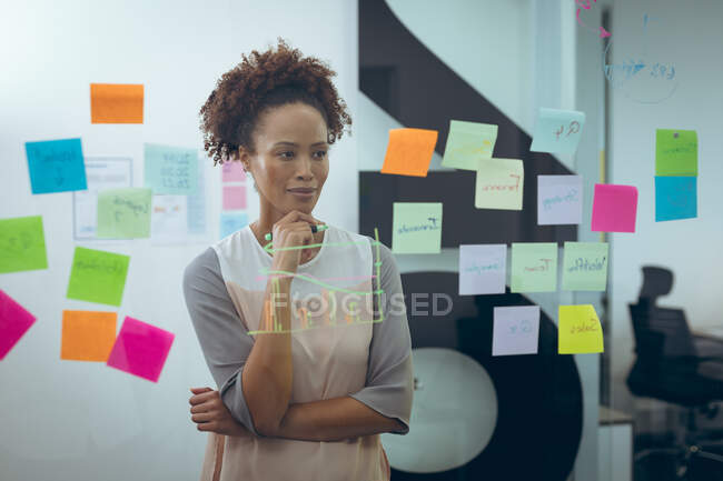 Una donna d'affari mista che prende appunti sulla lavagna di vetro e pensa. lavorare in un'attività creativa indipendente. — Foto stock
