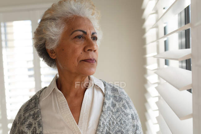 Змішана раса старша жінка дивиться через вікно. перебування вдома в ізоляції під час карантину . — стокове фото
