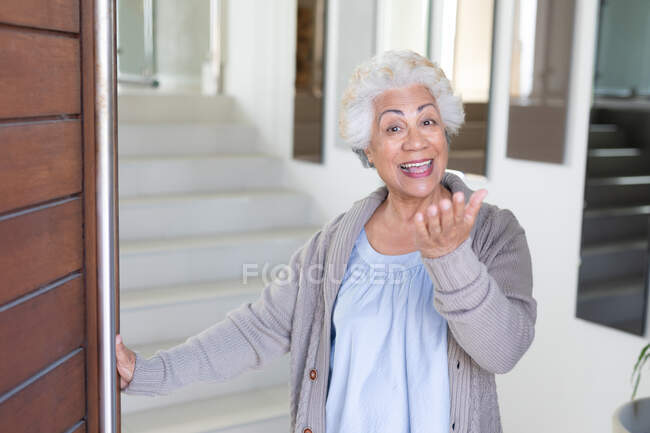 Retrato de mestiço de mulher idosa abrindo porta e sorrindo. ficar em casa em isolamento durante o confinamento de quarentena. — Fotografia de Stock