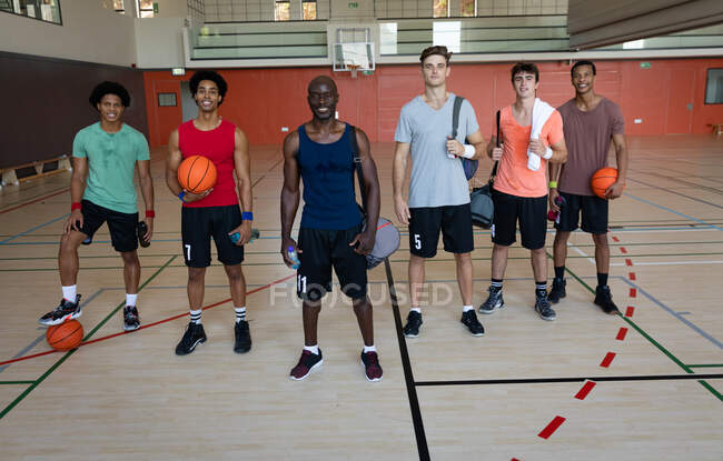 Portrait de diverses équipes masculines de basket-ball et entraîneur souriant et tenant des balles. basket-ball, entraînement sportif sur un terrain intérieur. — Photo de stock