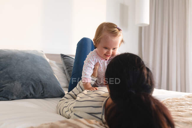 Retrato de mãe caucasiana brincando com seu bebê deitado na cama em casa. maternidade, amor e conceito de cuidado do bebê — Fotografia de Stock