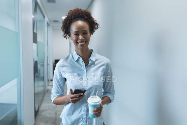 Porträt einer Geschäftsfrau mit gemischter Rasse, die lächelt und ihr Smartphone in der Hand hält. Arbeit in einem unabhängigen kreativen Unternehmen. — Stockfoto