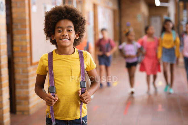 Retrato de un chico afroamericano sonriendo mientras estaba parado en el pasillo de la escuela. escuela y concepto de educación - foto de stock