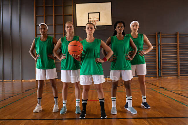 Retrato de un diverso equipo femenino de baloncesto usando ropa deportiva y sosteniendo la pelota. baloncesto, entrenamiento deportivo en una cancha cubierta. - foto de stock