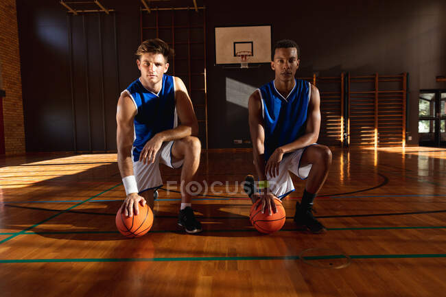Retrato de dos jugadores de baloncesto masculino diversos sosteniendo pelotas. baloncesto, entrenamiento deportivo en una cancha cubierta. - foto de stock
