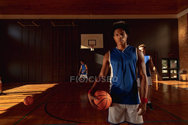 Портрет баскетболиста смешанной расы с командой на заднем плане. баскетбол, спортивные тренировки на крытой площадке. — стоковое фото