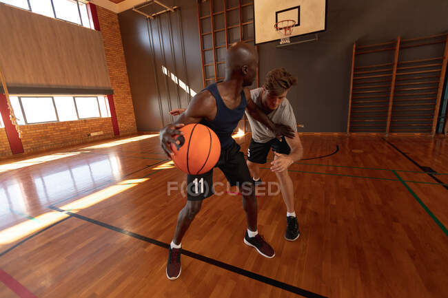Jugador de baloncesto masculino caucásico y entrenador practican driblar pelota. baloncesto, entrenamiento deportivo en una cancha cubierta. - foto de stock