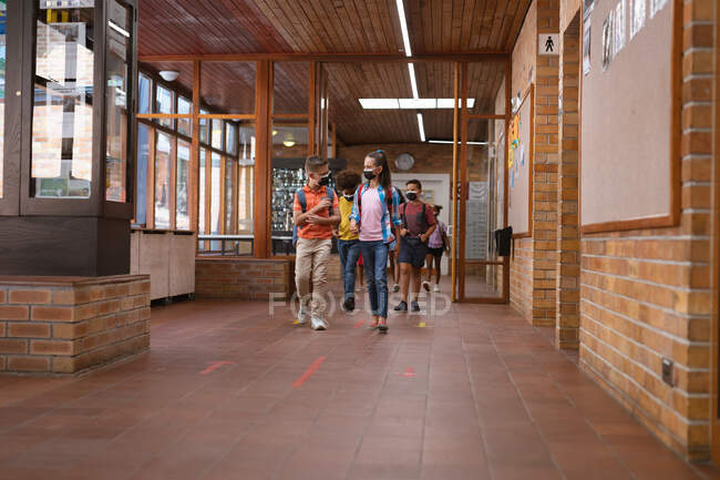 Eine Gruppe unterschiedlicher Schüler mit Mundschutz läuft auf dem Flur der Schule. Schul- und Bildungskonzept — Stockfoto