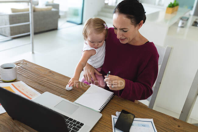 Caucasian mother holding her baby taking notes while working from home. motherhood, love and baby care concept — Stock Photo