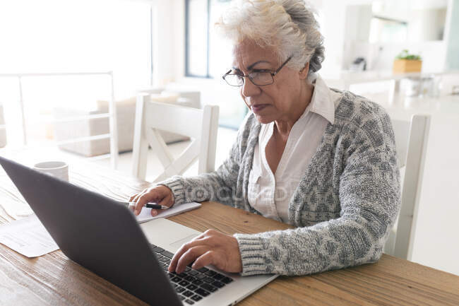 Gemischte Rasse Seniorin sitzt am Tisch mit Laptop. Isolationshaft während der Quarantäne. — Stockfoto