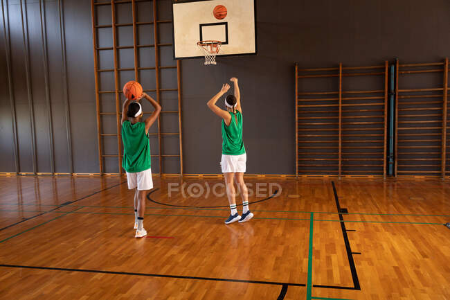 Two diverse female basketball players practicing shooting with ball. basketball, sports training at an indoor court. — Stock Photo
