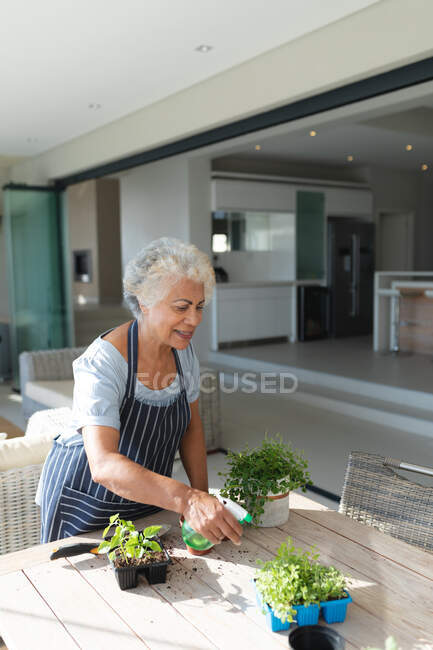 Mixed race senior woman gardening in living room. staying at home in isolation during quarantine lockdown. — Stock Photo